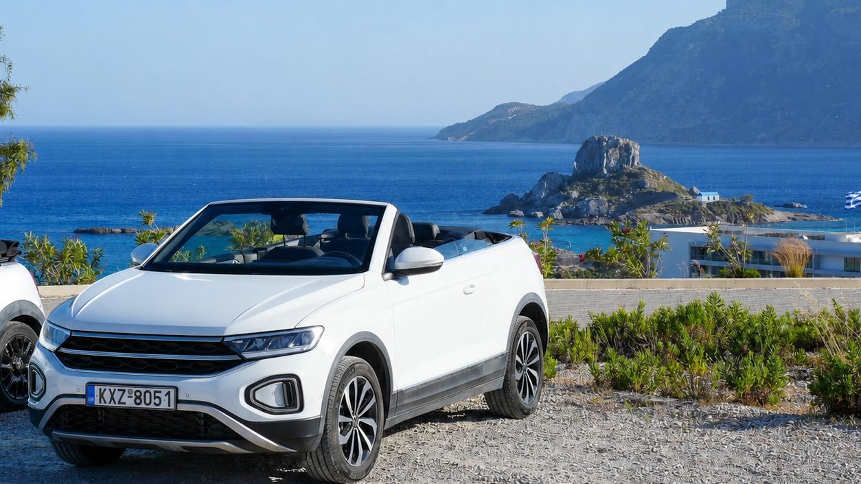 A white open-top hire car parked above the bay at Kefalos, with Kastri islet in the sea behind