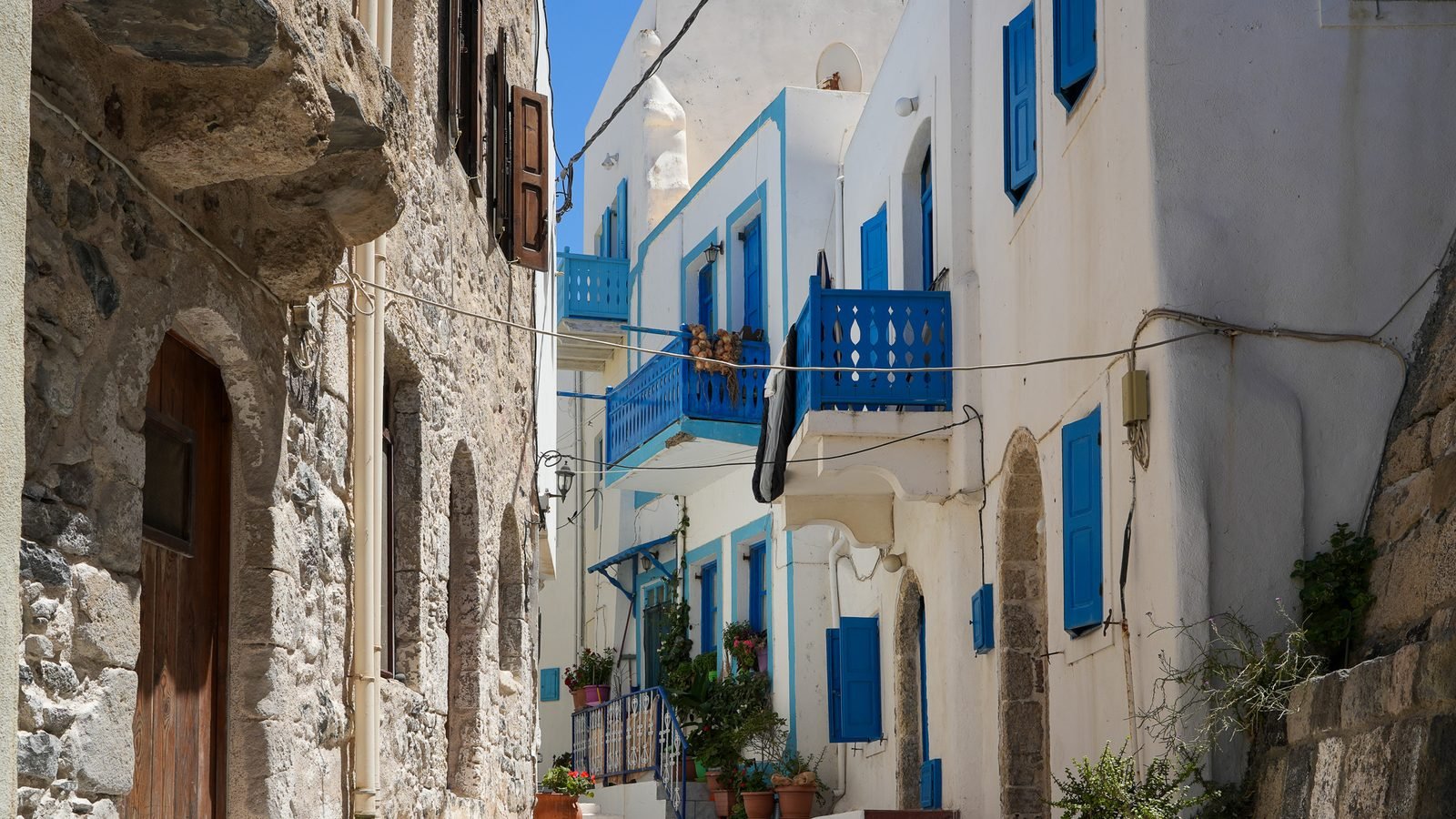 Ένα στενό ασβεστωμένο σοκάκι με γαλάζια παντζούρια και πέτρινα σκαλιά